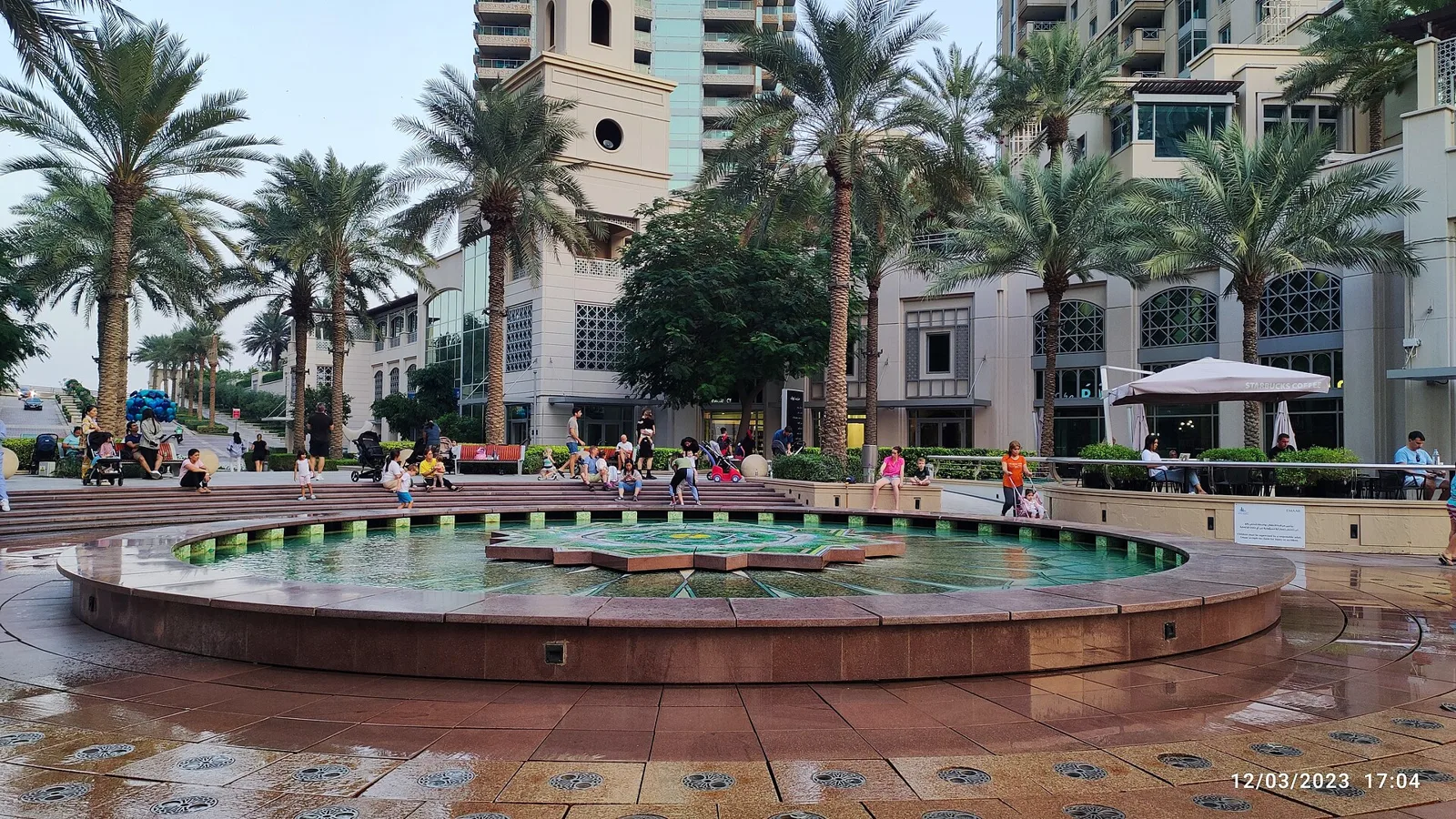Fountain and palm trees along Dubai Marina Walk with residential towers behind